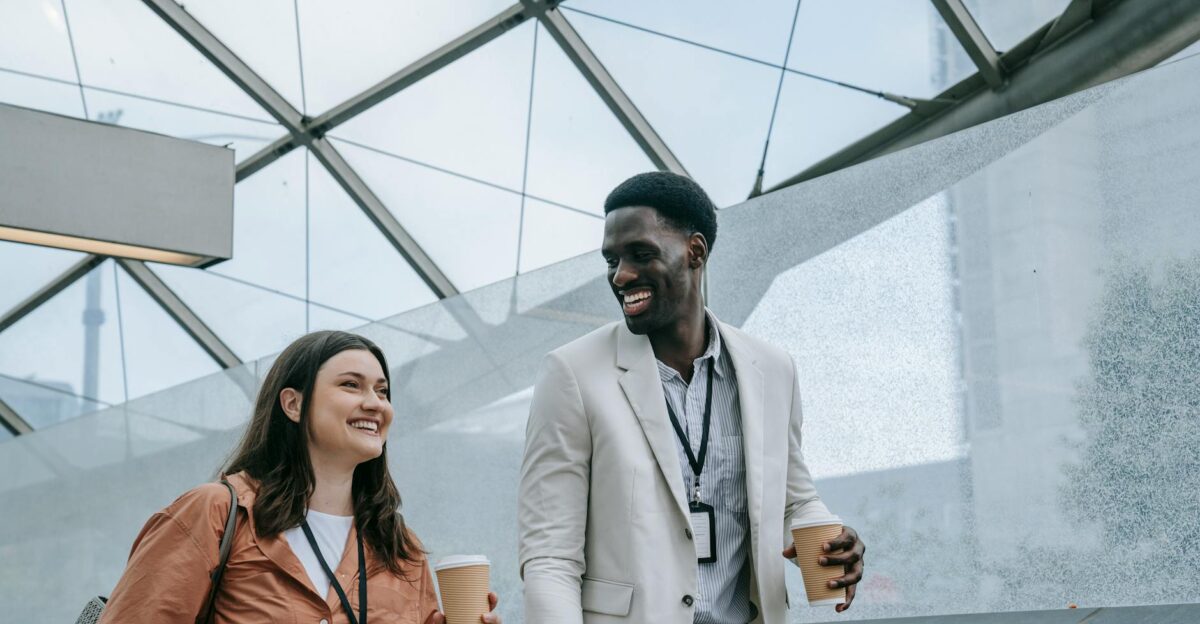 Smiling diverse colleagues walking indoors with coffee conveying professional camaraderie