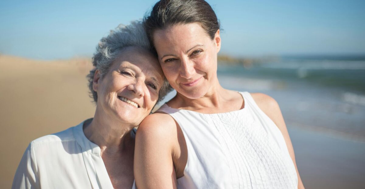 A senior mother and her adult daughter smiling together on a sunny beach in Portugal