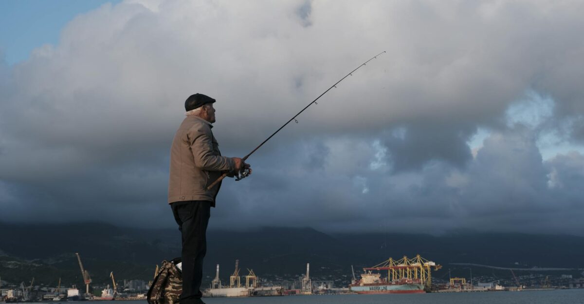 An elderly man fishing by Novorossiysk port amidst dramatic clouds