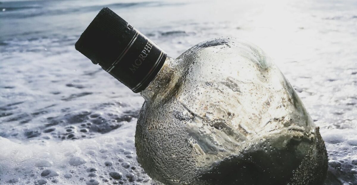 An empty bottle with seafoam washed ashore on a sunny beach captures travel and nature s essence