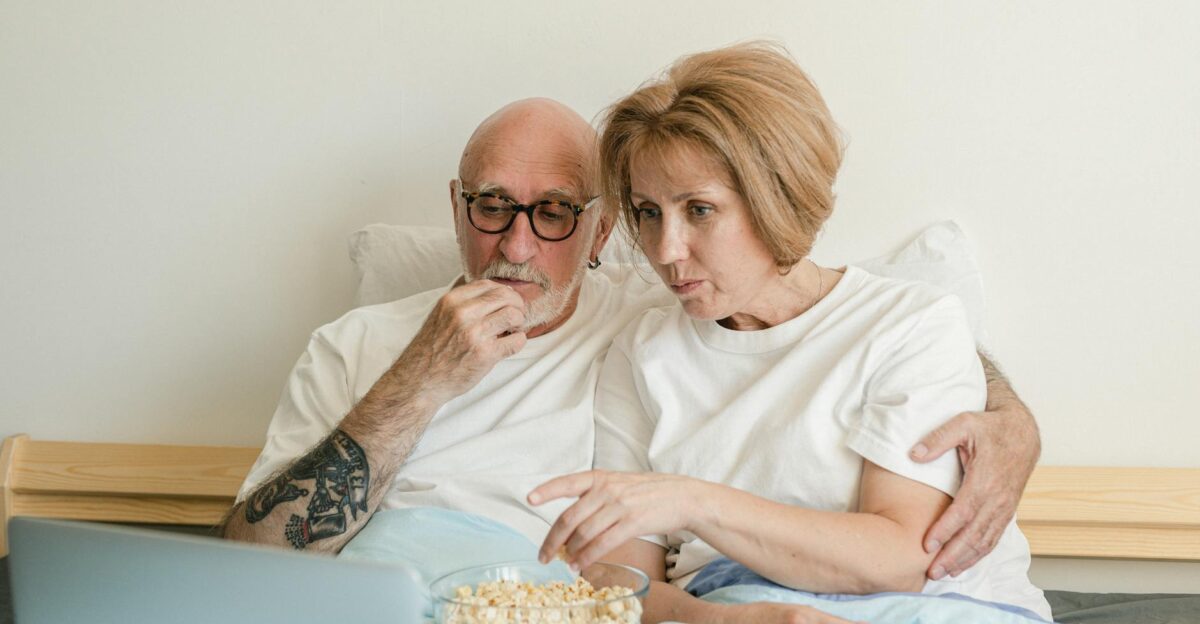 Senior couple bonding over movie night with popcorn and laptop in cozy home setting