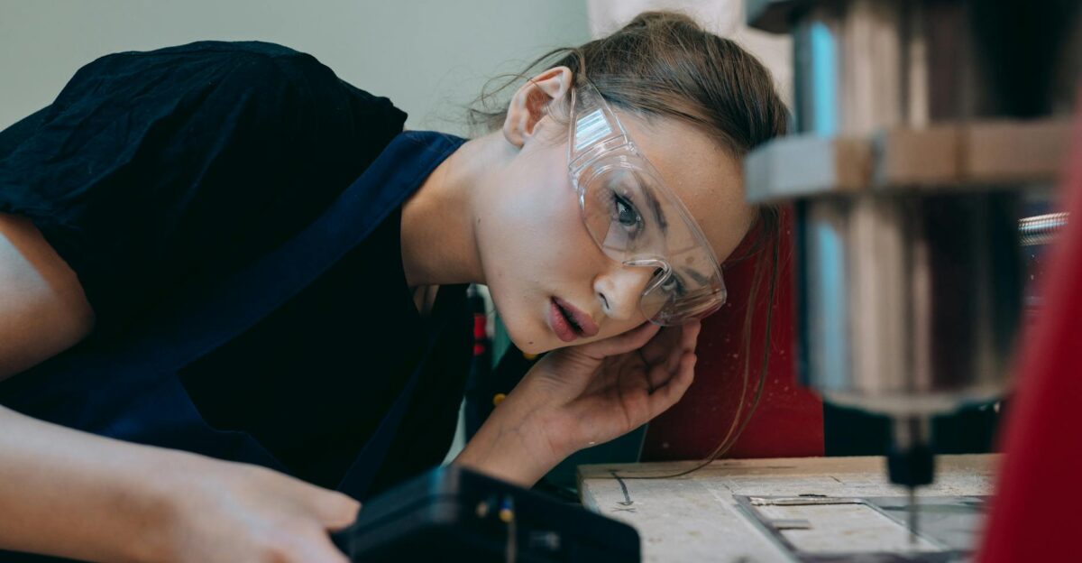 Young woman in workshop wearing goggles focusing on machinery operation