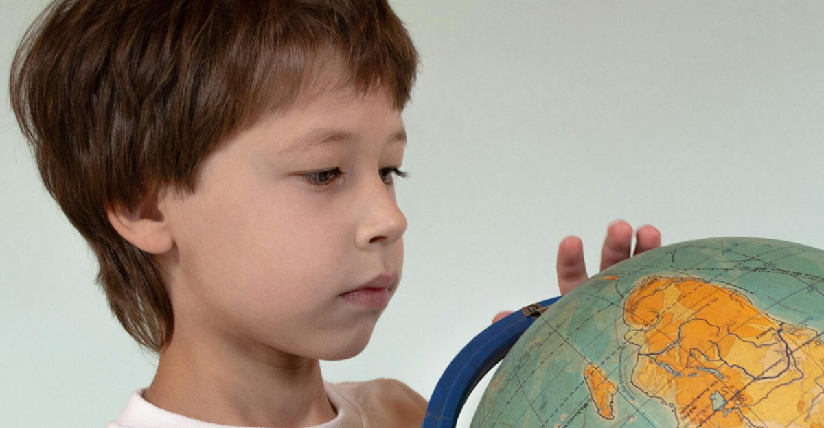 A young boy examines a desk globe indoors, fostering curiosity and learning about geography.