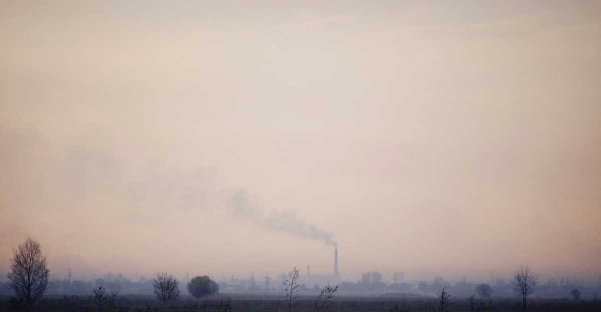 A factory chimney emitting smoke into a foggy sky over a desolate landscape
