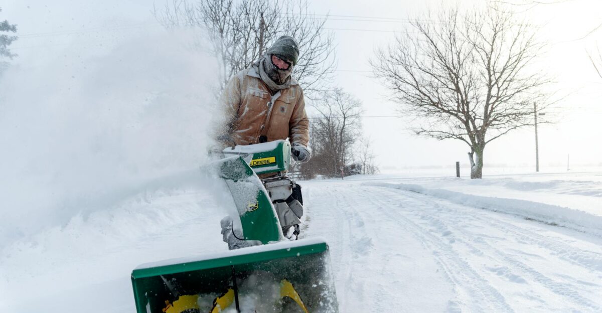 Man using a snow blower to clear snow during winter in Essex ON under cold weather conditions