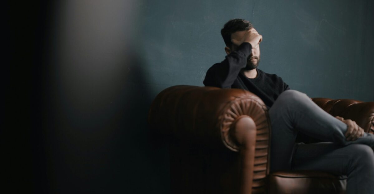 a man holds his head while sitting on a sofa