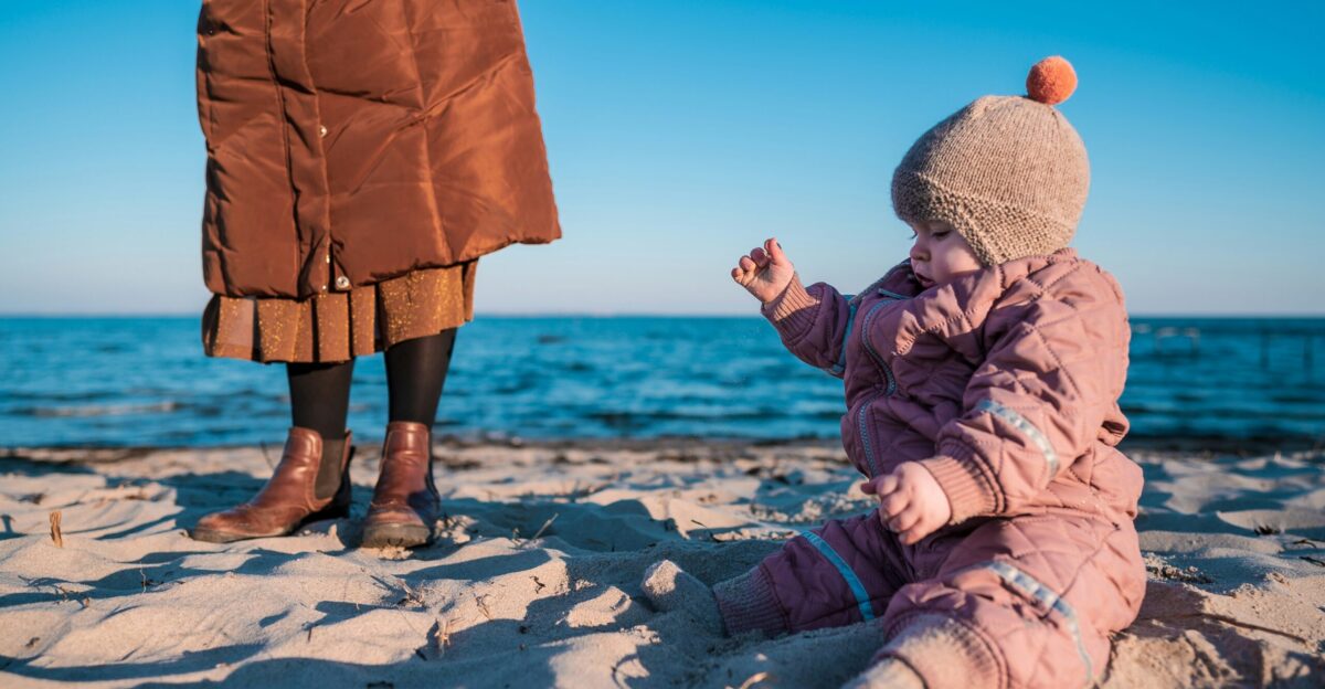 child in brown jacket and gray knit cap sitting on white snow covered ground during daytime