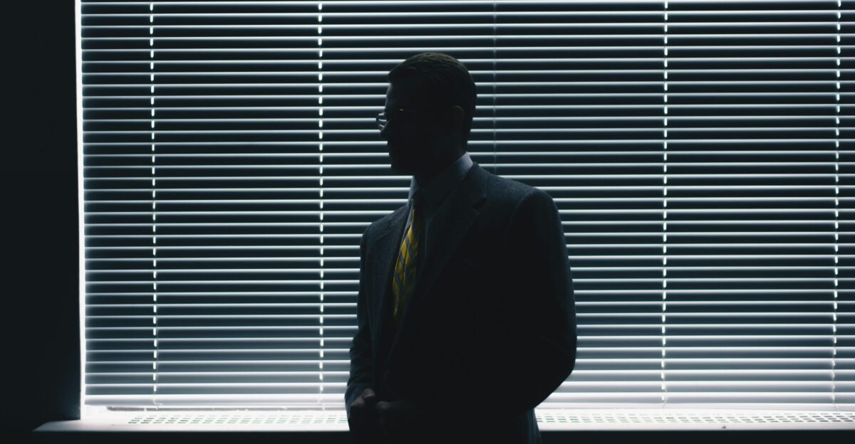 man in black suit standing near window blinds