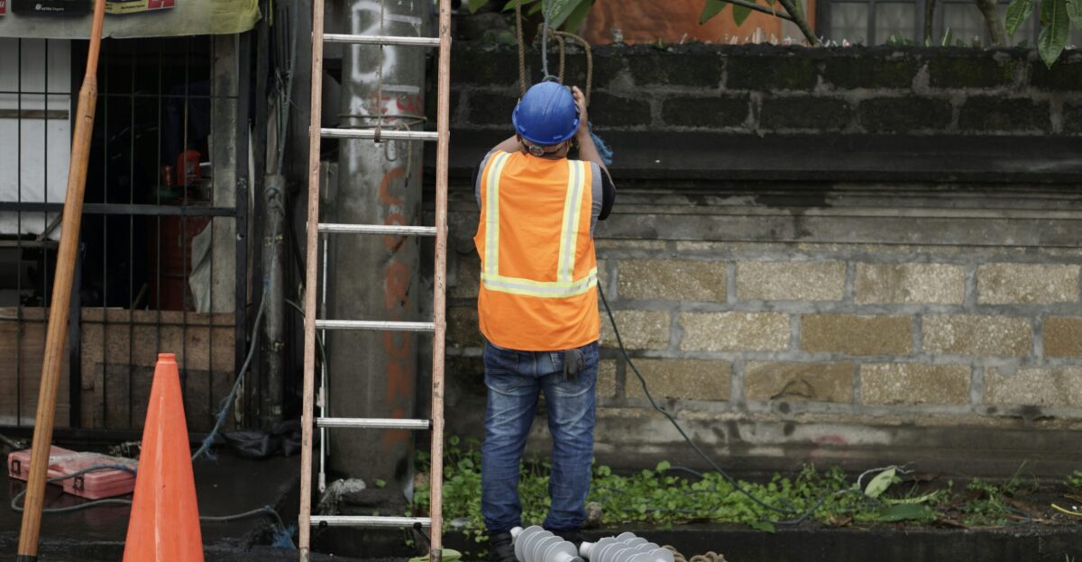 a man in an orange vest and safety vest standing next to a ladder