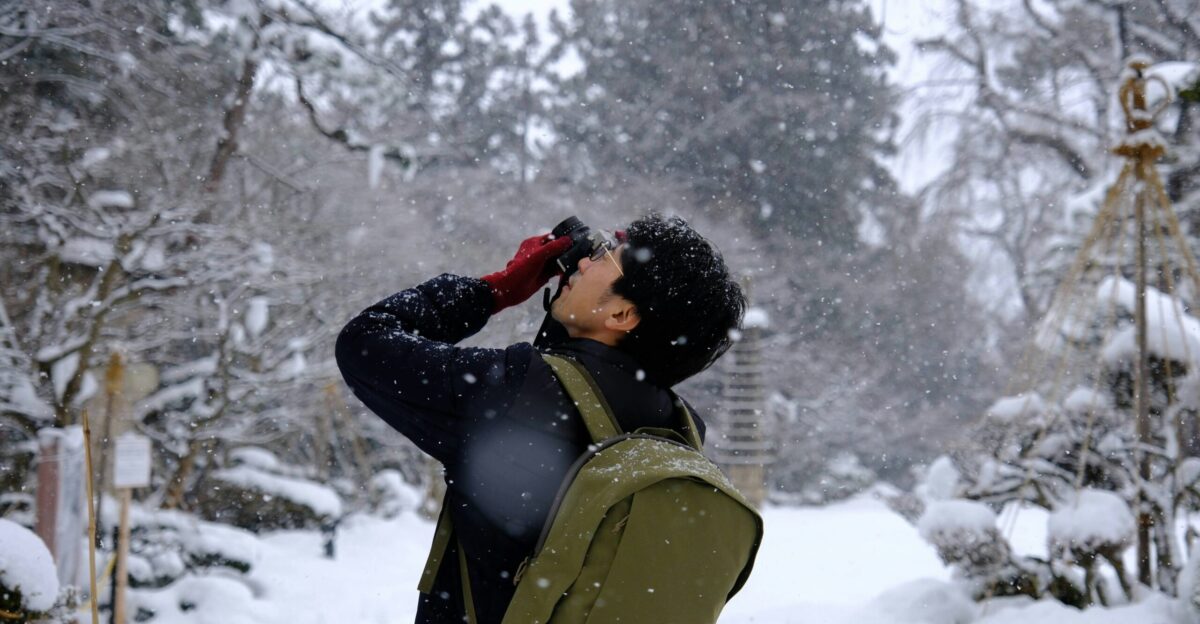 a man standing in the snow looking through a pair of binoculars