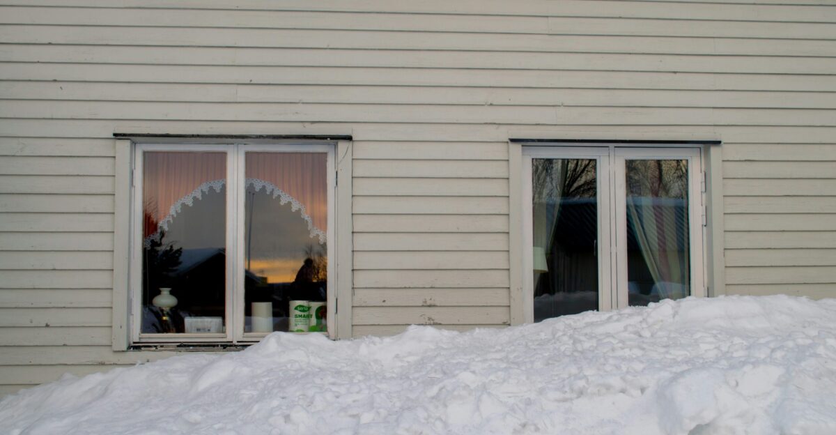 a white house with two windows and a pile of snow