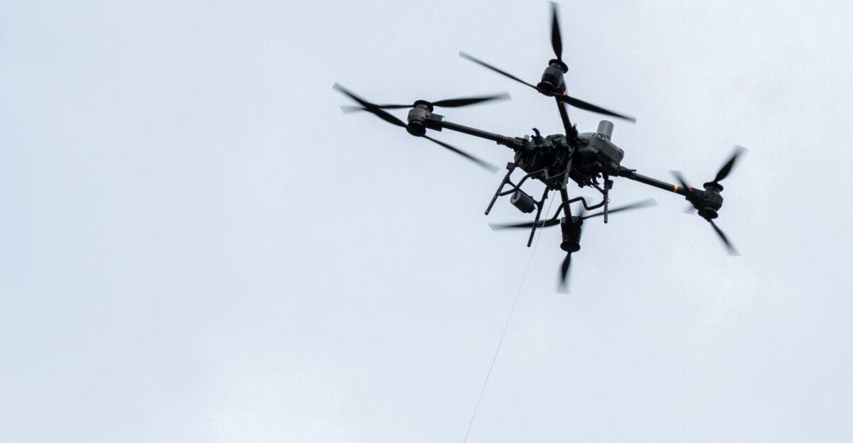 A drone flies high against a cloudy sky