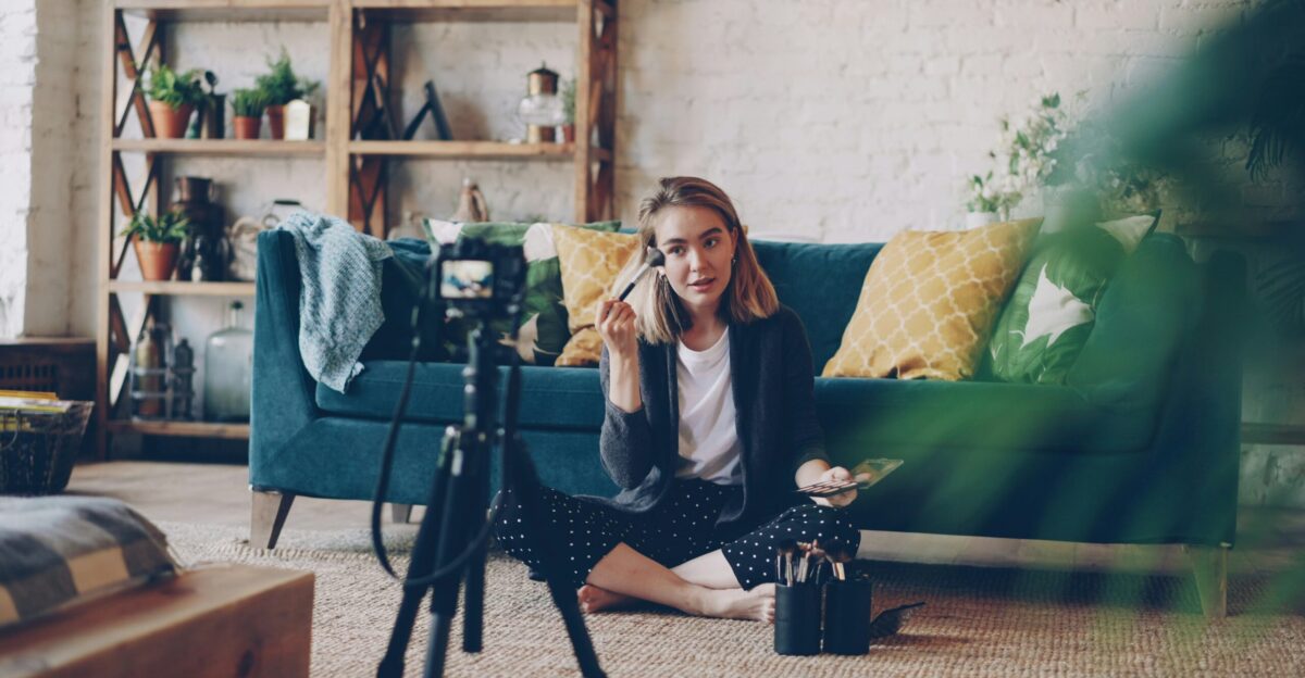 Woman applying makeup for camera in living room