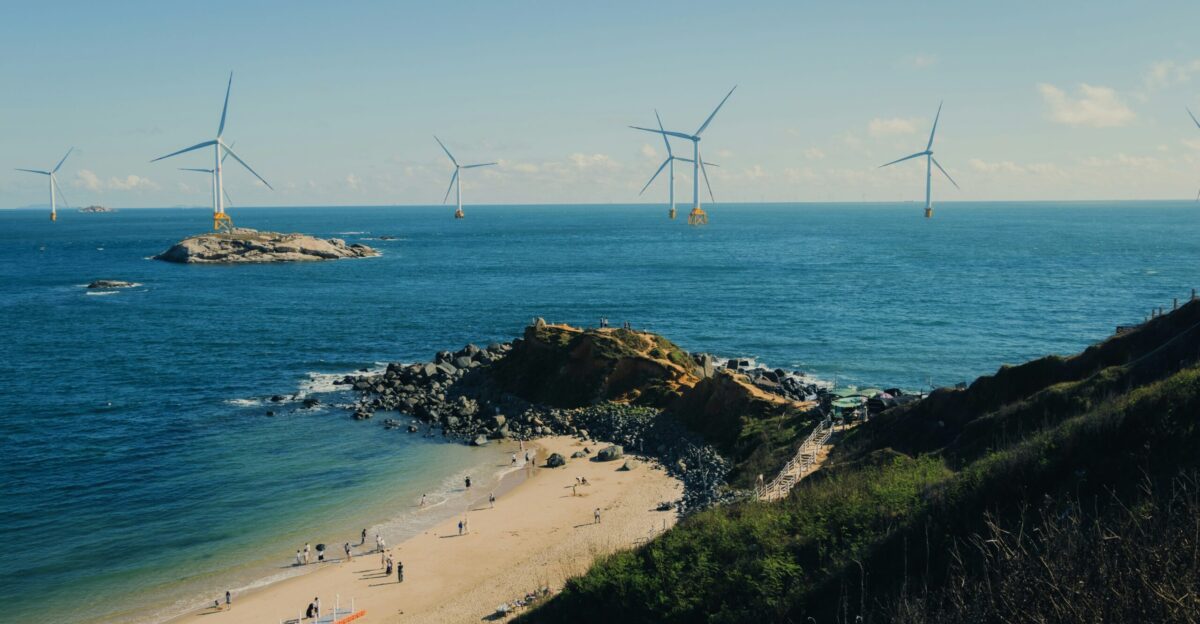 Wind turbines at sea near a rocky coastline and beach