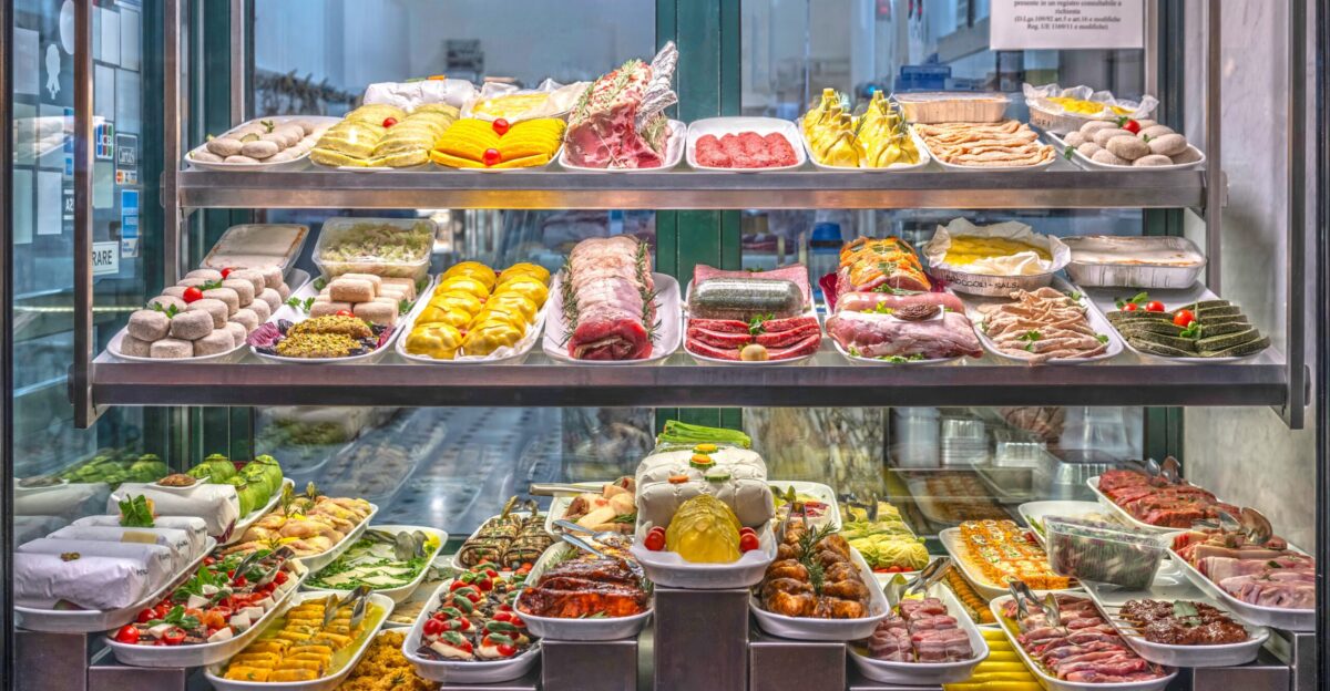 Shop window of an Italian delicatessen in Rome showcasing a wide variety of prepared foods and traditional Italian products The display includes cured meats cheeses stuffed pasta cooked dishes and fresh vegetables all arranged neatly on trays inside a refrigerated glass case The vibrant presentation reflects the richness and visual appeal of Italian cuisine
