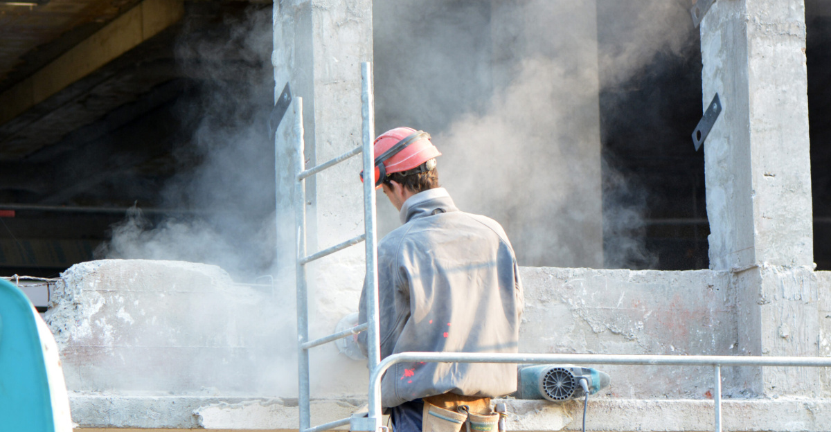 Cloud of dust and worker without mask and without hearing protection during a rehabilitation project (Lille, Northern France). Inhaling this type of dust exposes a risk of silicosis or other lung diseases.