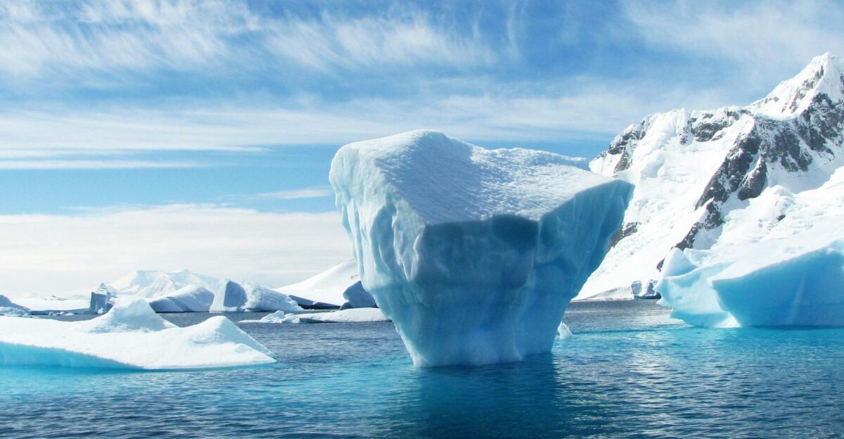 A stunning iceberg floating in the cold pristine waters with a backdrop of snowy mountains