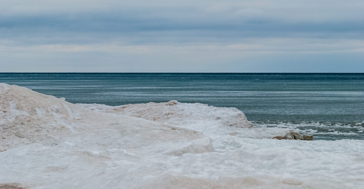 Snow on a Lake Michigan shoreline contrasts deep blues of the lake and sky