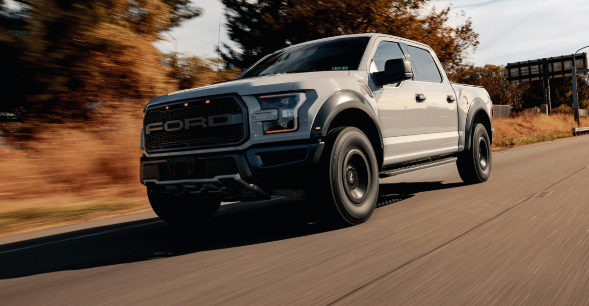 A Ford F-150 driving on a scenic highway surrounded by trees and blue skies.