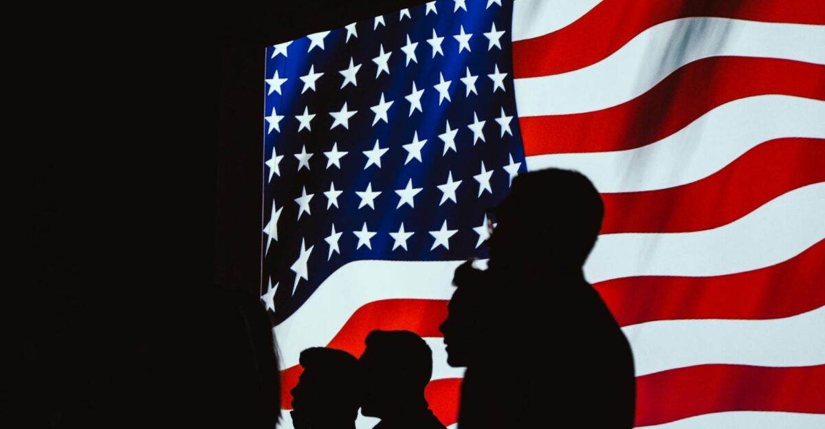 Silhouetted figures in front of a bright wavy American flag create a patriotic scene