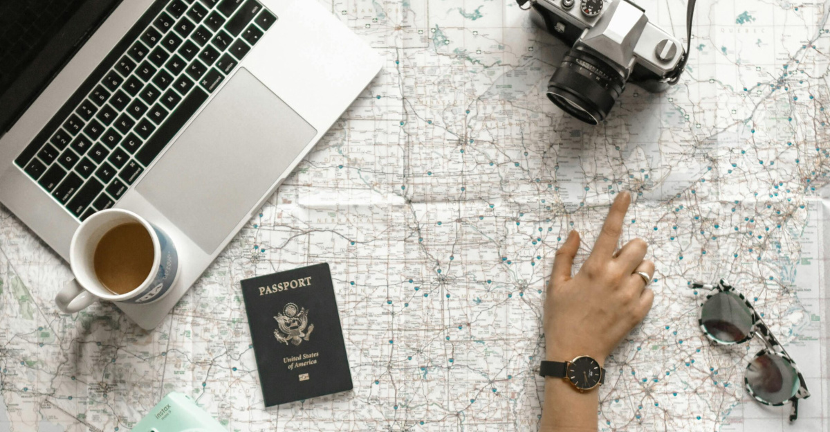 Hand on map with camera, passport, laptop, and coffee, perfect for travel planning inspiration.