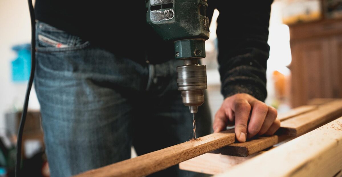Close-up of a person using an electric drill on a wooden plank showcasing detailed woodworking skills