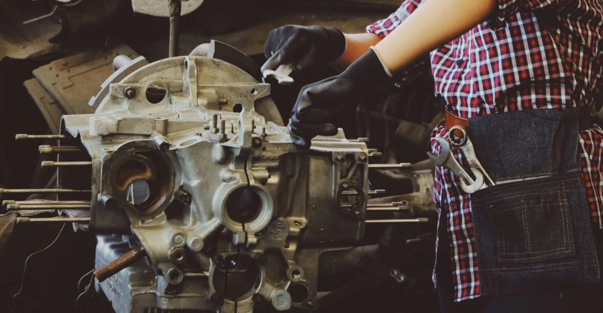Woman engineer wearing safety gear, working on machine repair in an industrial setting.