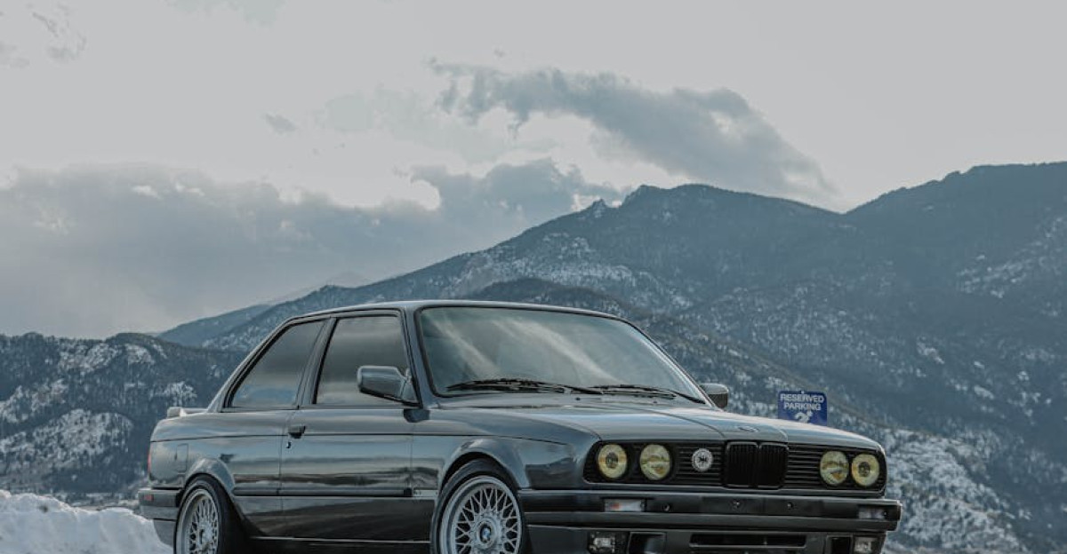 Classic car parked on a scenic mountain road with snow-capped peaks in the background