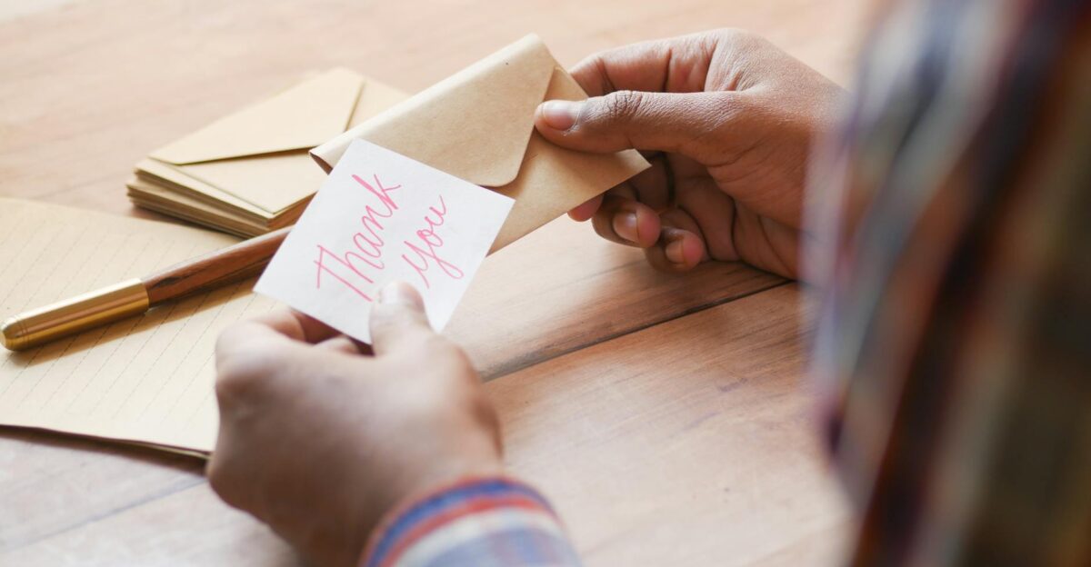 Close-up of hands holding a thank you note in an envelope on a table