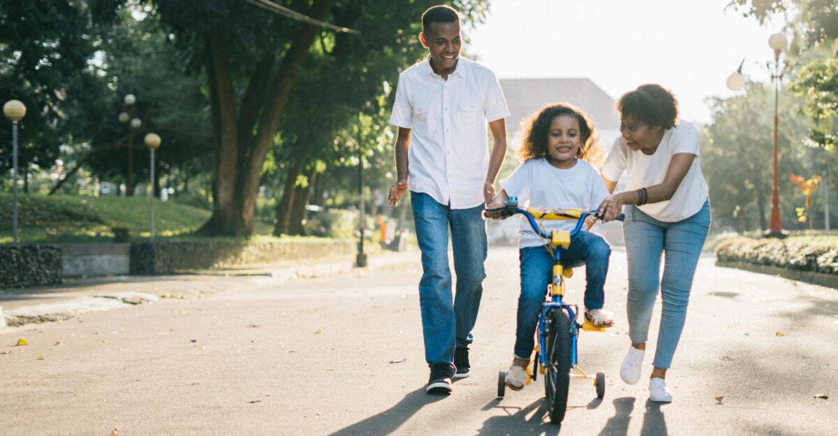 Happy family teaching their child to cycle on a sunny day outdoors