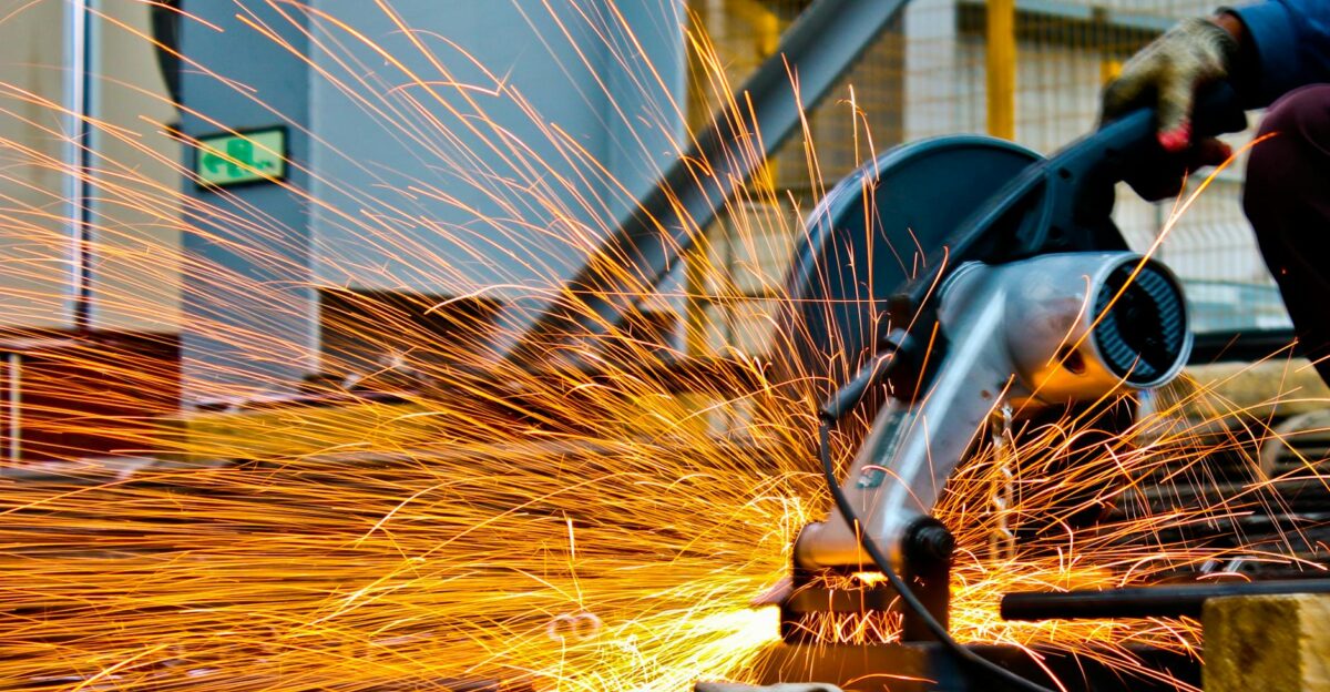 A worker operates a grinder cutting metal creating a vibrant display of sparks in an industrial setting