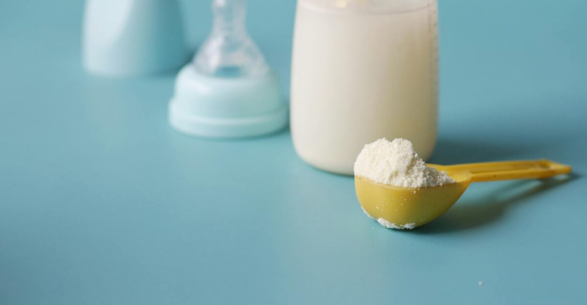 Close-up of baby milk formula powder in a yellow scoop with a bottle on a blue background