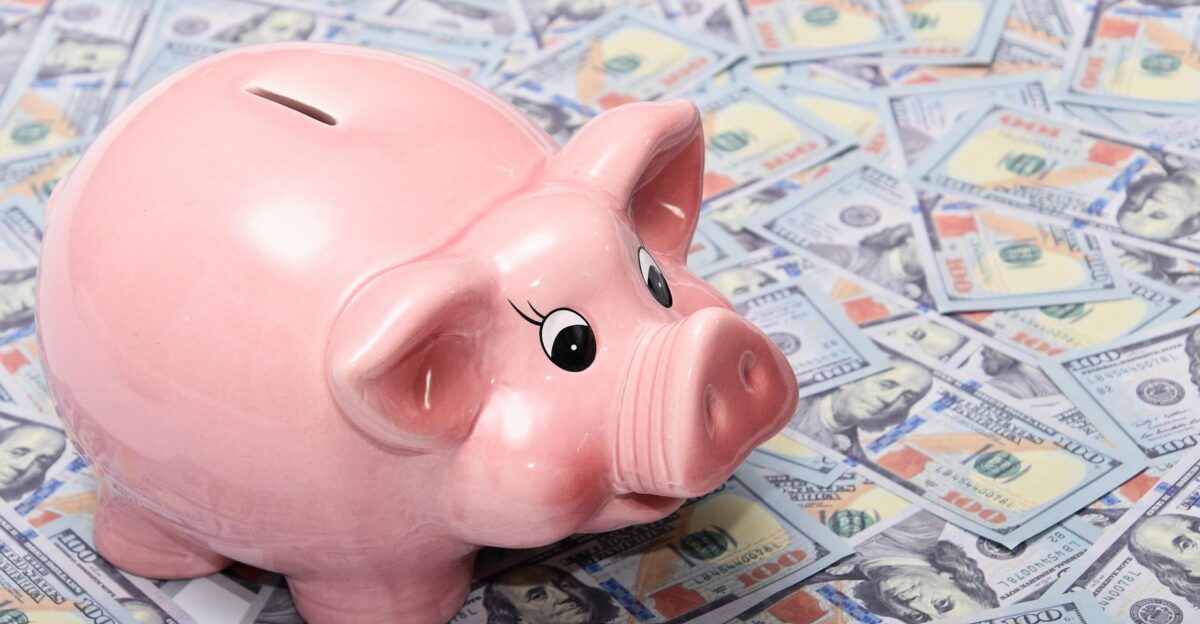 Pink ceramic piggy bank placed on a spread of US dollar bills symbolizing savings and financial security
