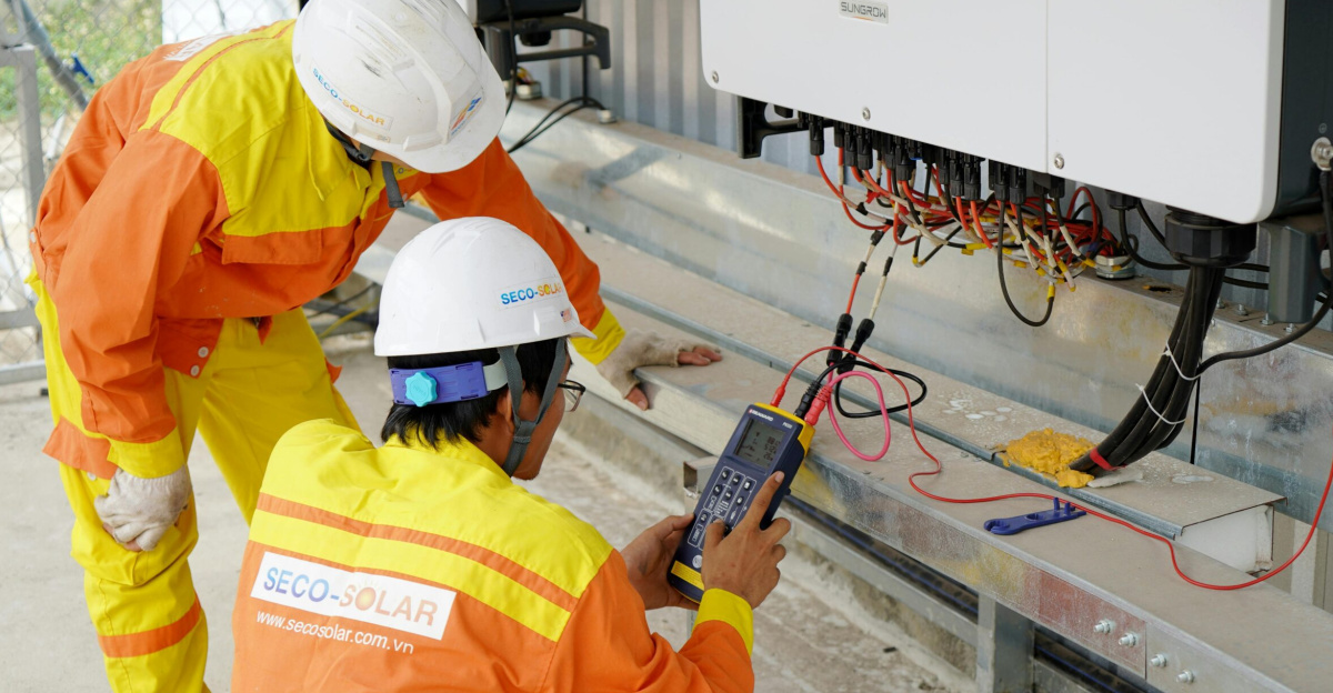 Two electrical engineers installing and testing solar power systems wearing safety gear at a construction site.