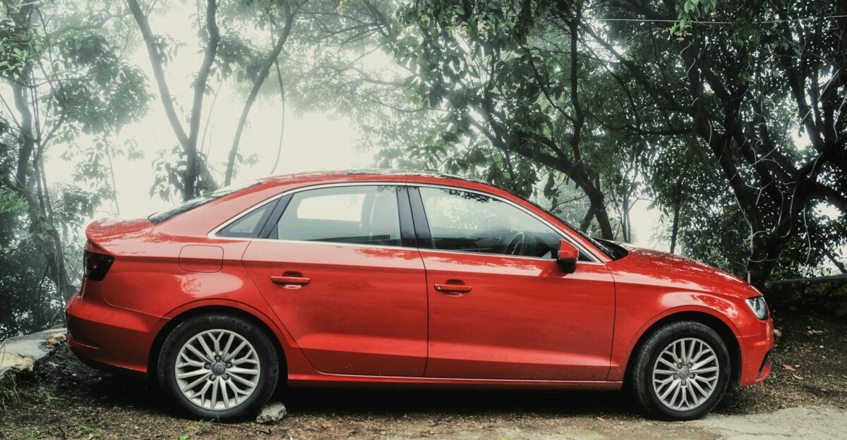 A vibrant red sedan parked amidst lush greenery on a foggy day showcasing elegance