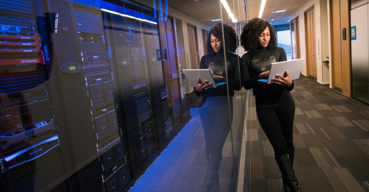 A woman using a laptop navigating a contemporary data center with mirrored servers