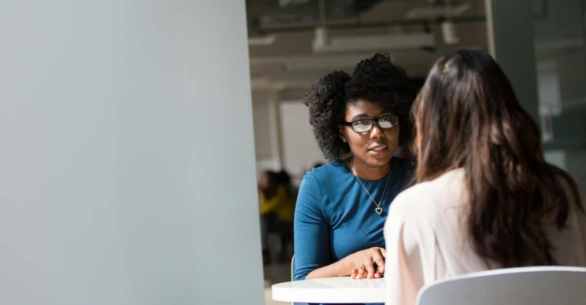 Two women engaged in a discussion in a modern office environment, highlighting communication and interaction.