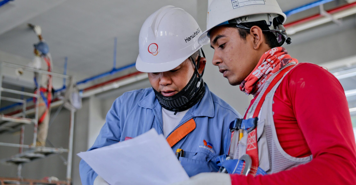 Two engineers in safety helmets reviewing construction plans at a worksite.
