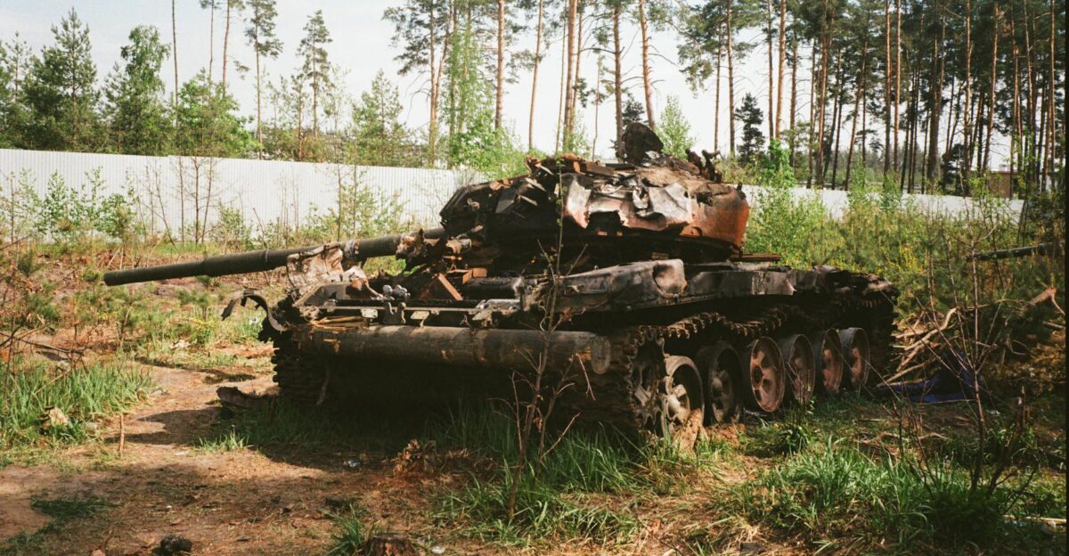 A destroyed military tank lies abandoned in a forest near Bucha Ukraine amidst war-torn surroundings