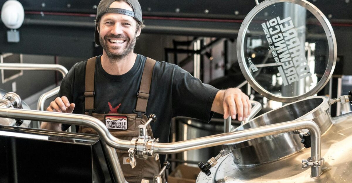 Happy brewer in a craft brewery standing near stainless steel equipment