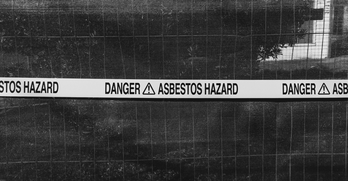 Black and white photo of an asbestos hazard warning sign on a fence.
