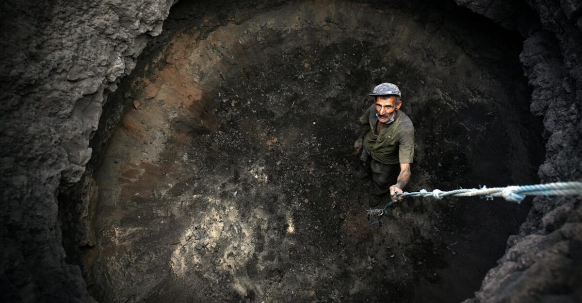 A man stands in a deep pit holding a rope looking up from a high angle view