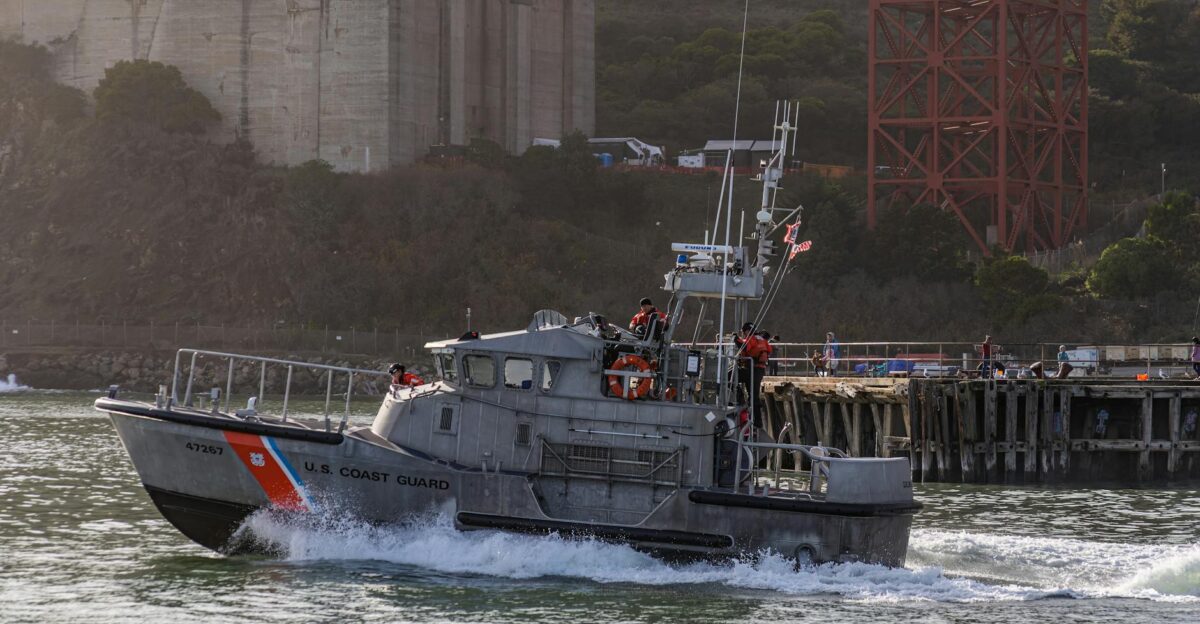 US Coast Guard boat navigating near a pier with coastal scenery in the background