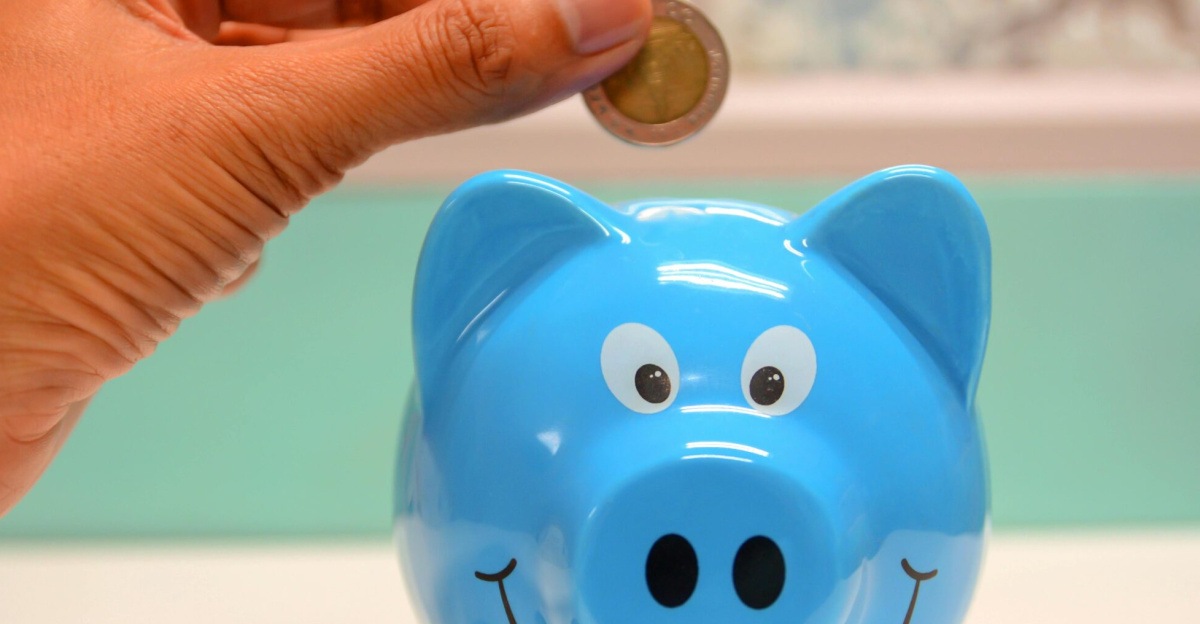Hand inserting a coin into a blue piggy bank for savings and money management.