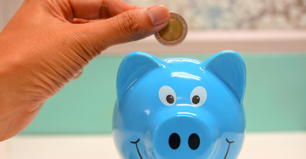 Hand inserting a coin into a blue piggy bank for savings and money management.