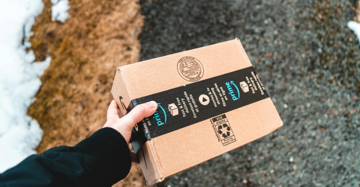 A person holding a cardboard Amazon Prime package on a snowy urban sidewalk