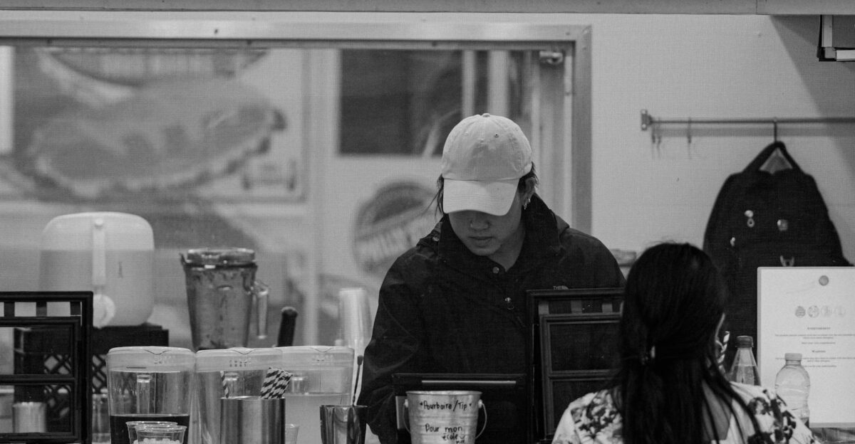Black and white image of a street food vendor in a window serving a customer