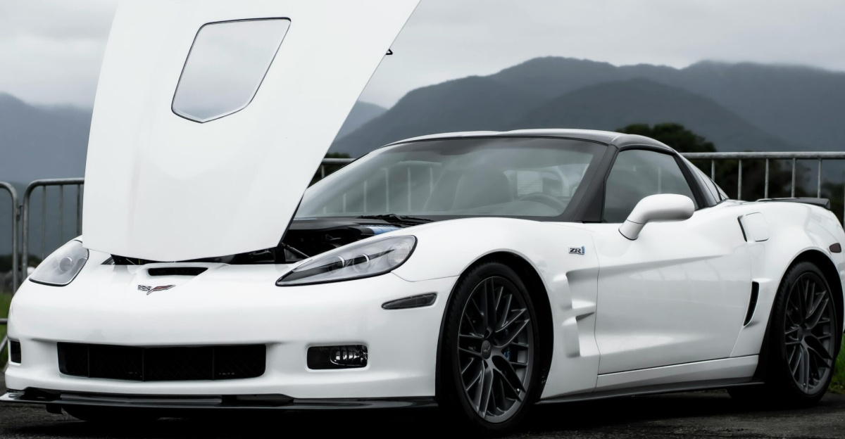 Front view of a white Chevrolet Corvette sports car with open hood against a mountainous backdrop.