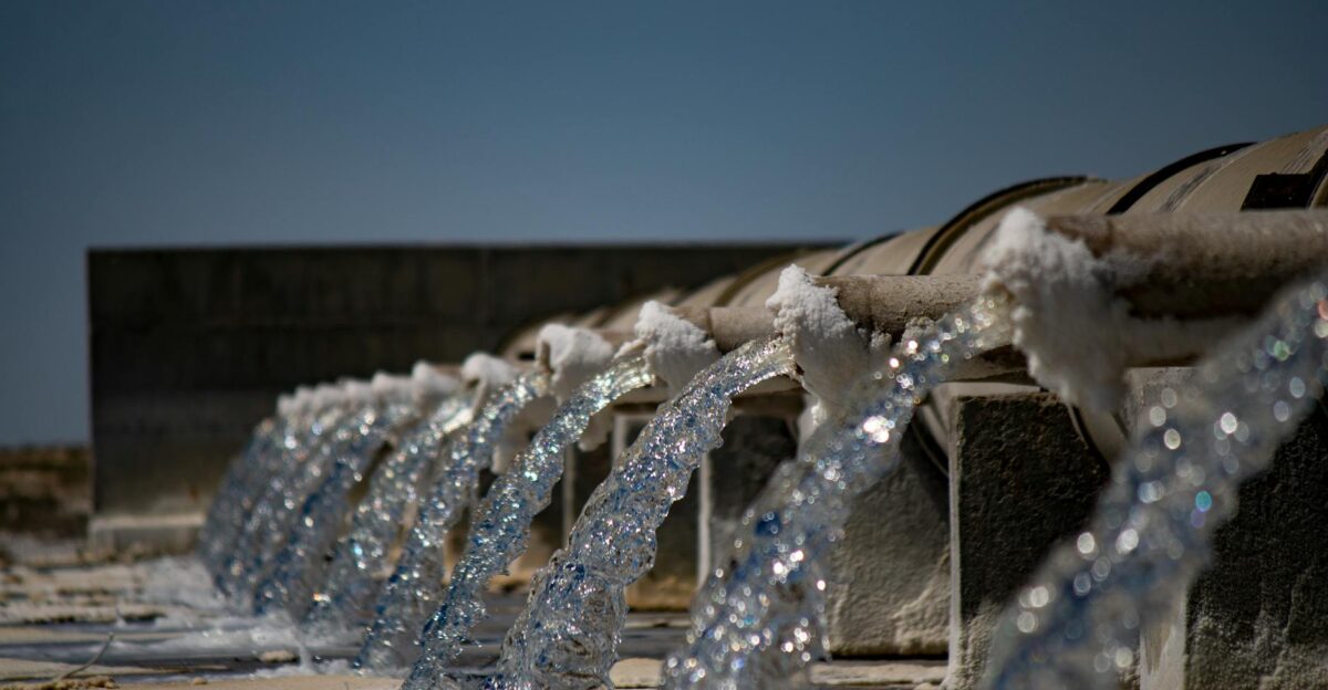 Close-up view of water flowing from industrial pipes against a clear blue sky