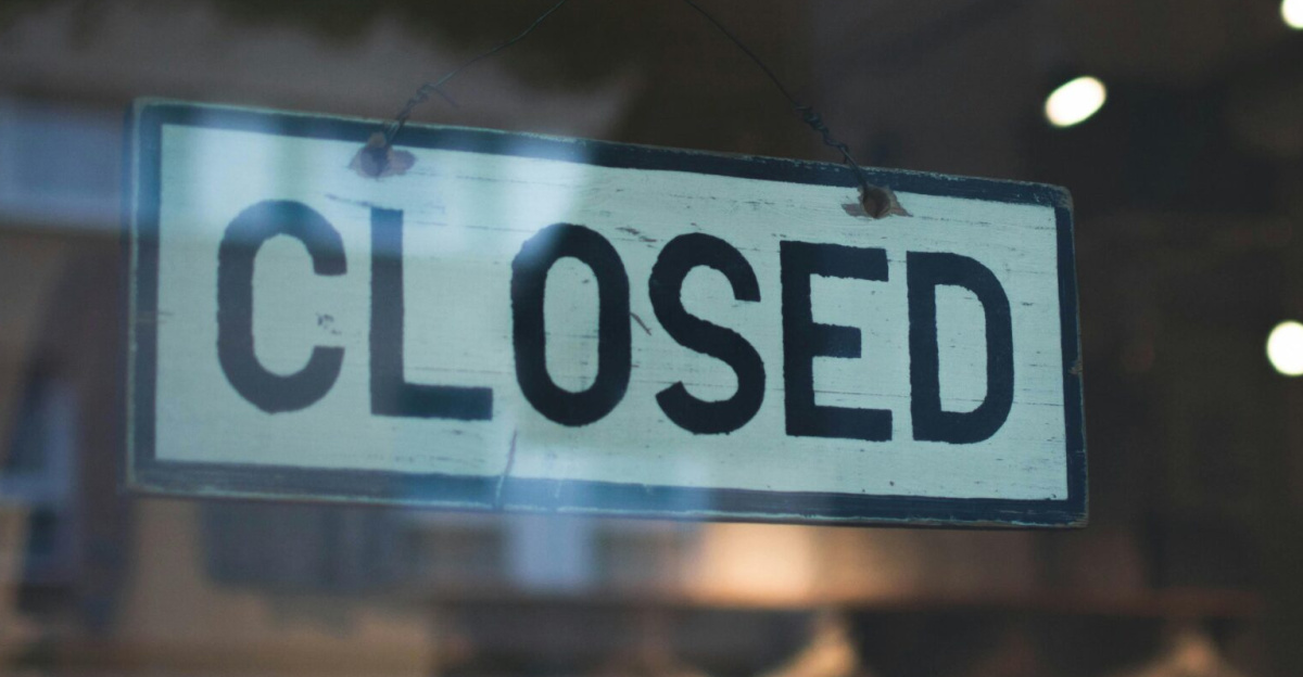 A closed sign hangs on a glass window of a modern urban storefront.